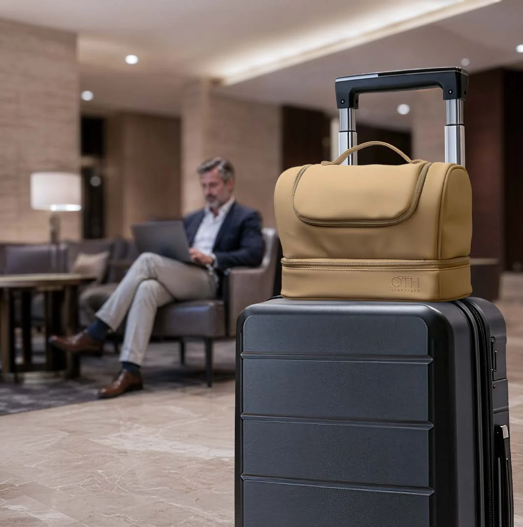 Trousse Over There sable sur une valise, dans un salon de voyage